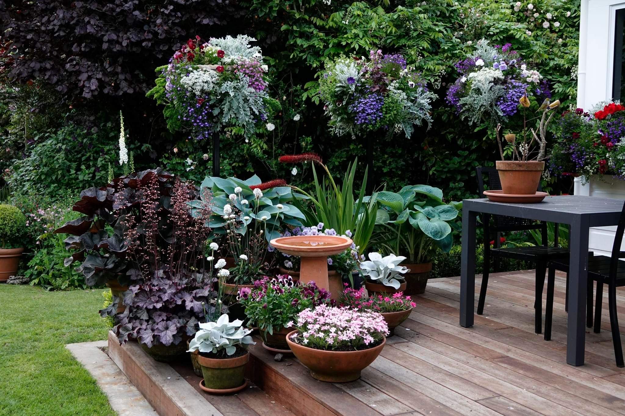 A wooden tiled garden patio with a variety of potted plants and garden furniture