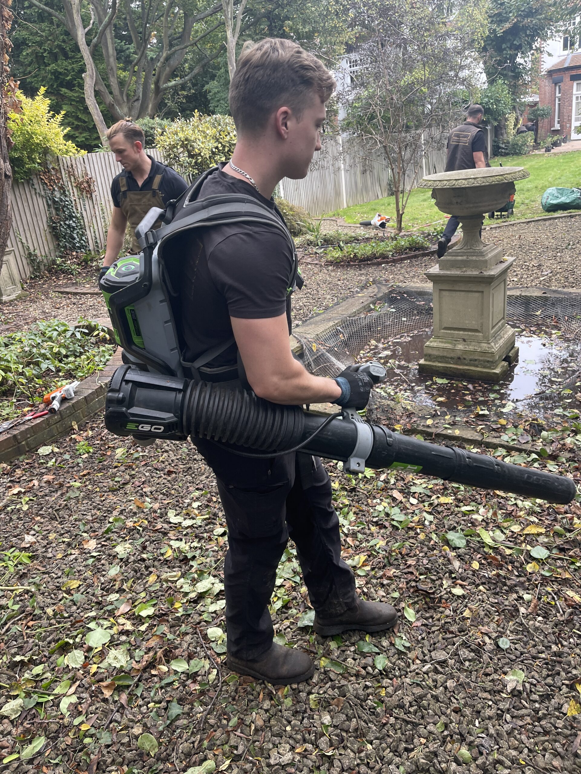 A Willow Alexander Gardens team member using a leaf blower in a garden