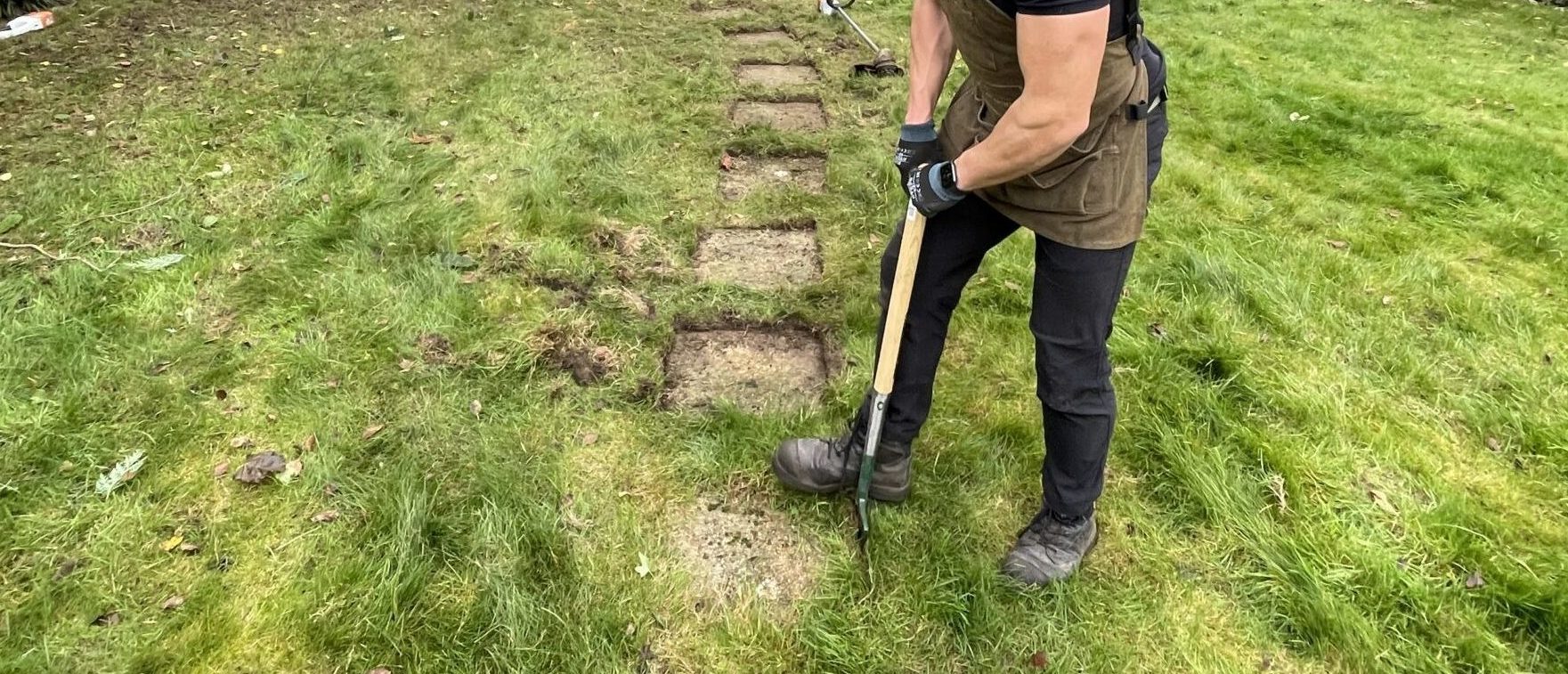 A member of the Willow Alexander Gardens team removing excess grass around a stone tile in a garden
