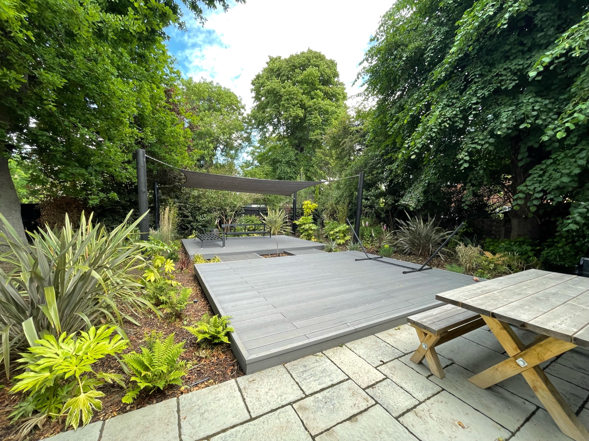 A neatly arranged garden with a tiled patio leading onto silver wooden decking designed by Willow Alexander