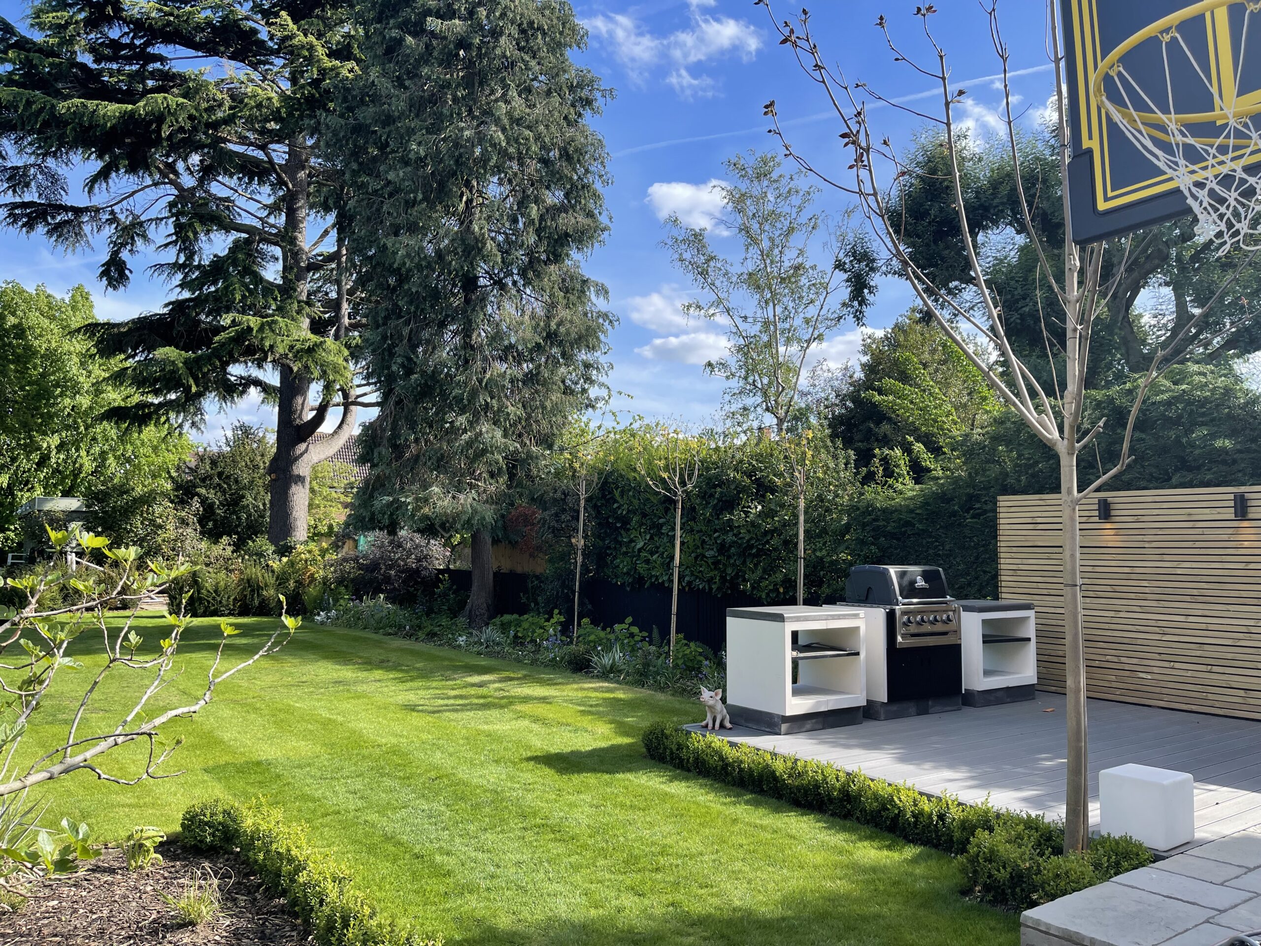A well-maintained garden lawn with a grey wooden decking featuring an outdoor grill and cooking area designed by Willow Alexander